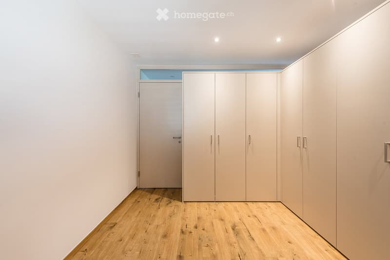 Empty room with light-colored wooden flooring, white walls, built-in closet units, and a small window above the door.