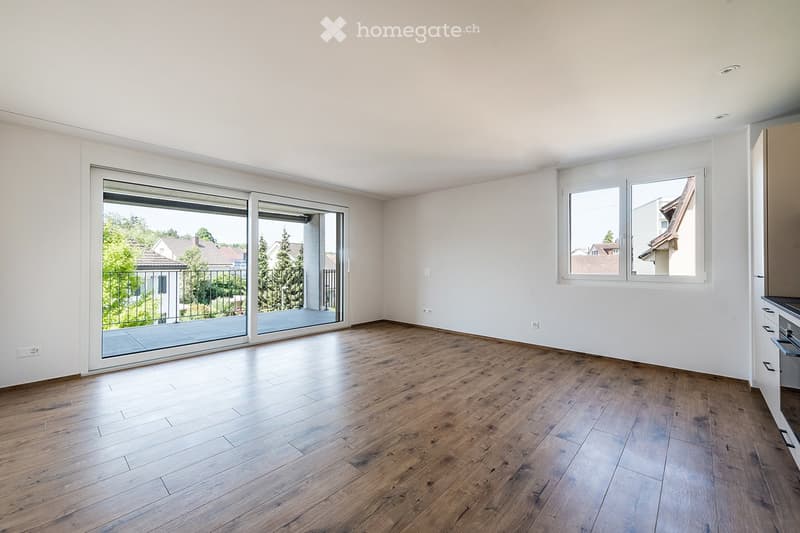 Empty room with wooden flooring, white walls, large sliding glass doors leading to a balcony, and windows with white frames.