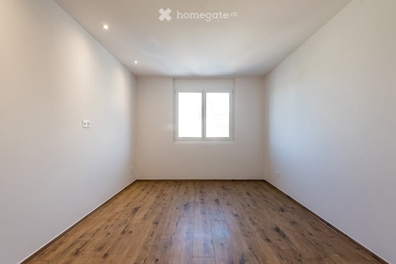 Empty room with wooden flooring, white walls, and a large window with double glass panels.