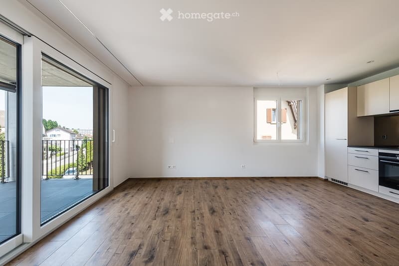 Empty room with wooden flooring, white walls, large window, and sliding glass door leading to a balcony.
