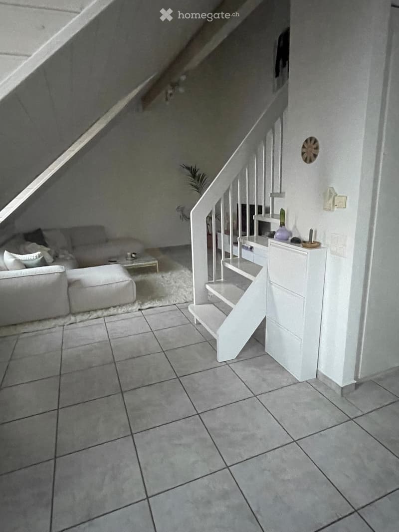 Modern, minimalist living room with white sofa, ottoman, coffee table, and a small staircase leading to an upper level.