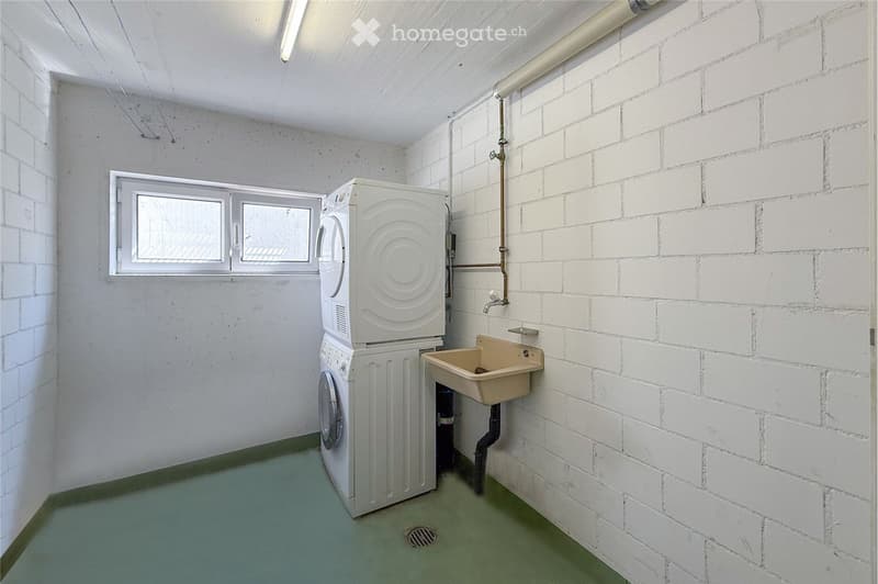 A small bathroom with white brick walls, a green floor, a window, a washing machine, and a sink.