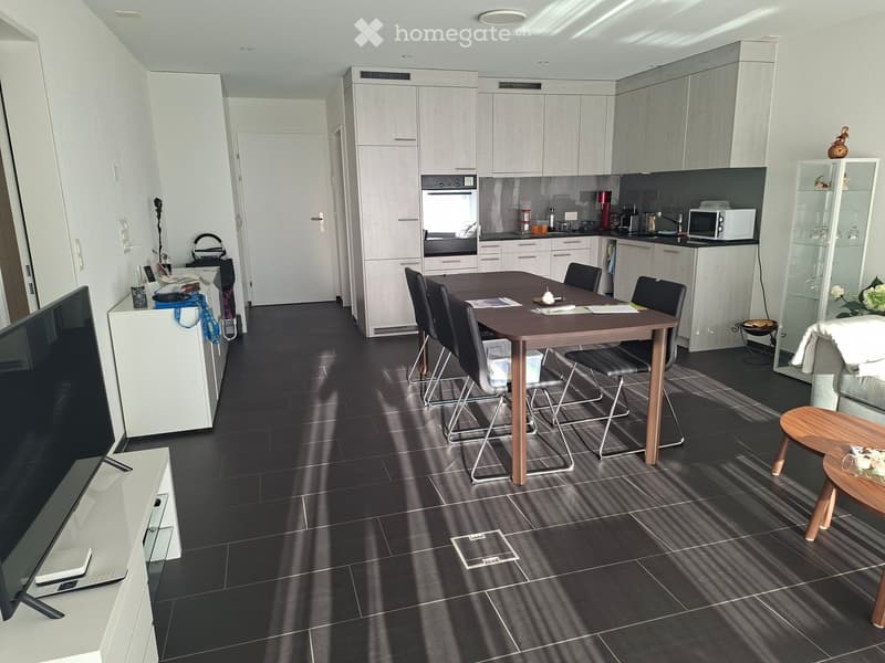 Modern open-plan living and dining area with dark tiled flooring, white cabinets, a dining table with chairs, a sofa, and a TV stand.