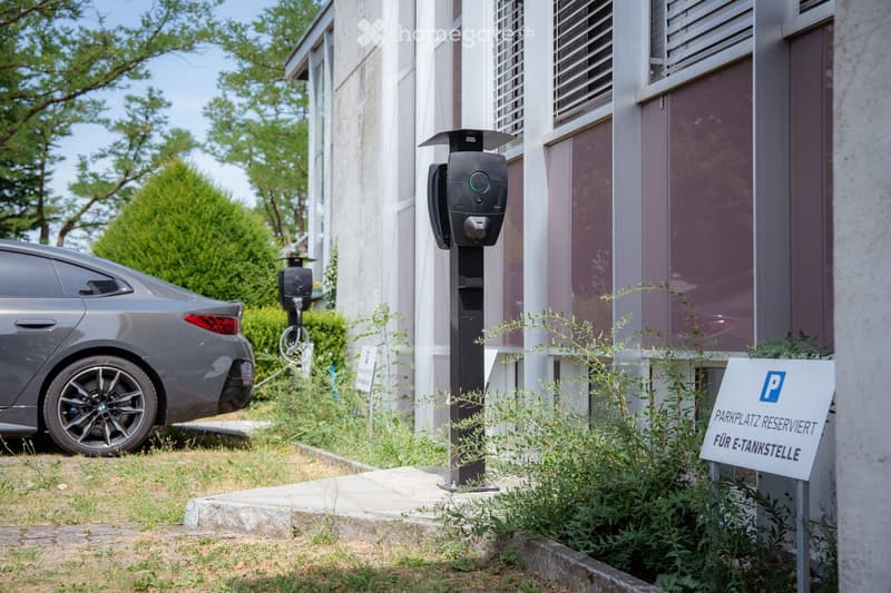 A modern building with a parking area featuring an electric vehicle charging station and a sign indicating a reserved parking spot for electric vehicles.