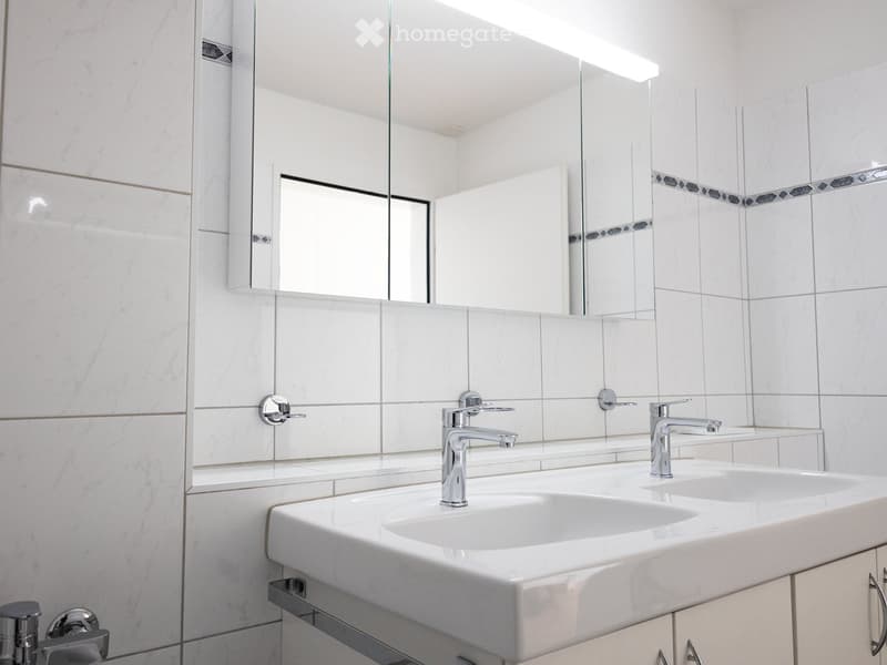 Modern bathroom with white marble tiles, double sink, sleek chrome faucets, and a large mirrored cabinet.