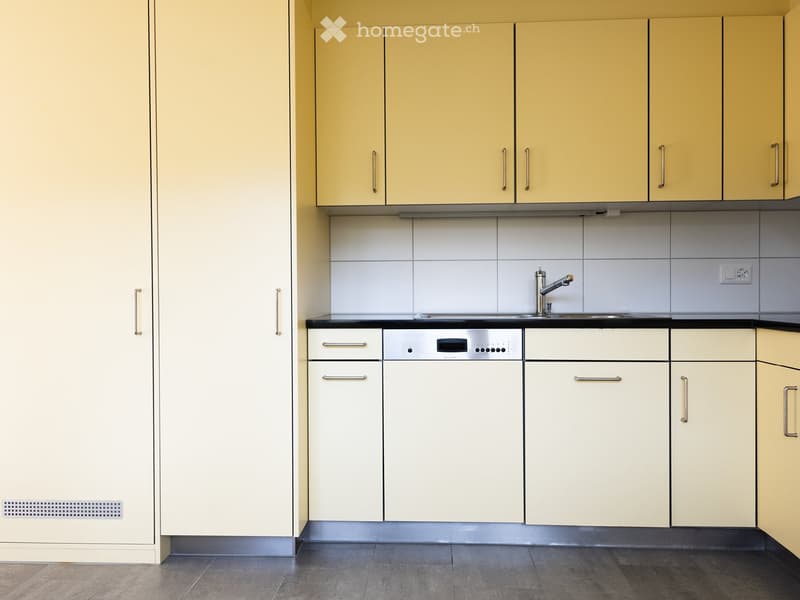 Modern kitchen with light-colored cabinets, stainless steel appliances, and a black countertop.