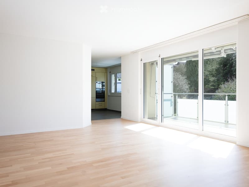 Empty room with light wooden flooring, white walls, and large glass sliding doors leading to a balcony area.