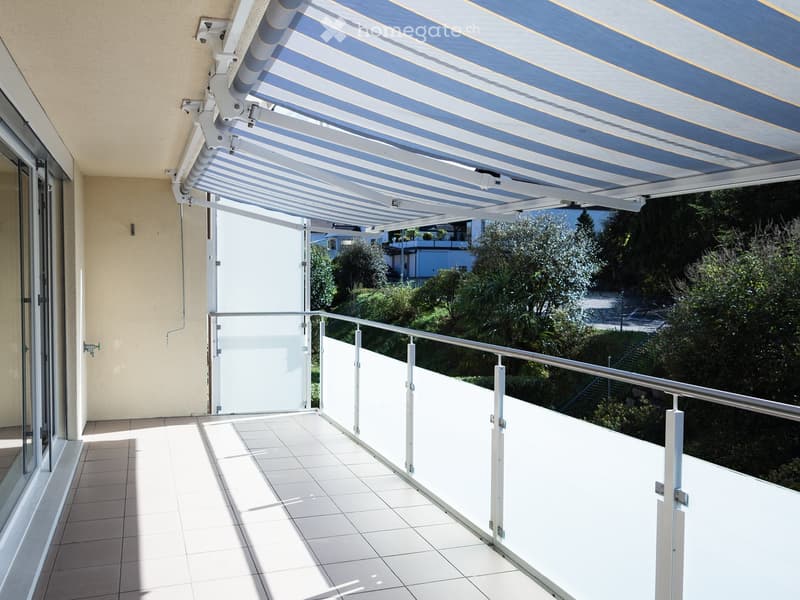 Balcony with white tiled floor, glass railing, and retractable awning providing shade.
