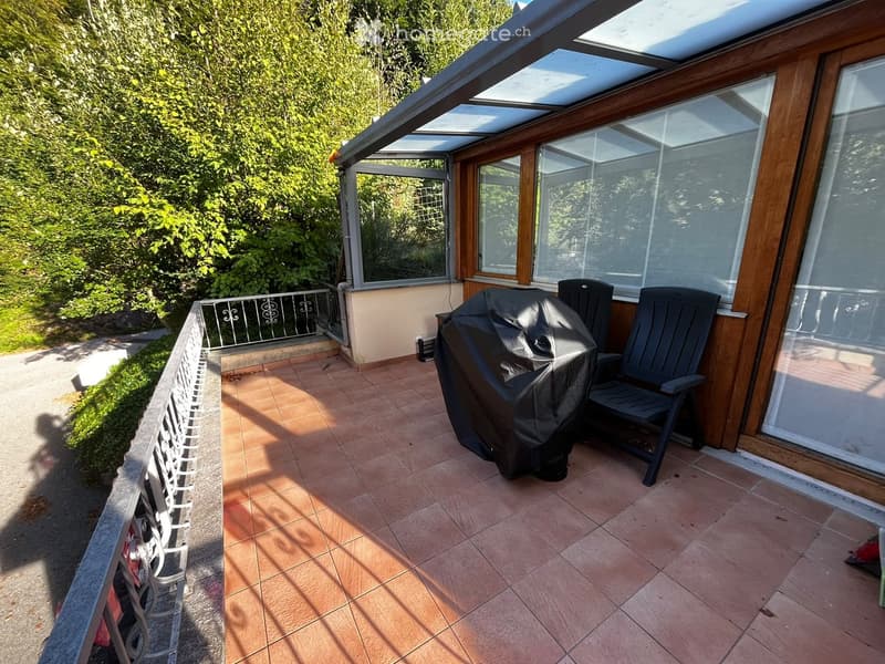 Balcony with tiled floor, covered area, grill, and chairs.