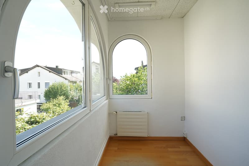 Empty room with wooden flooring, white walls, large arched windows, radiator, and a door handle visible.