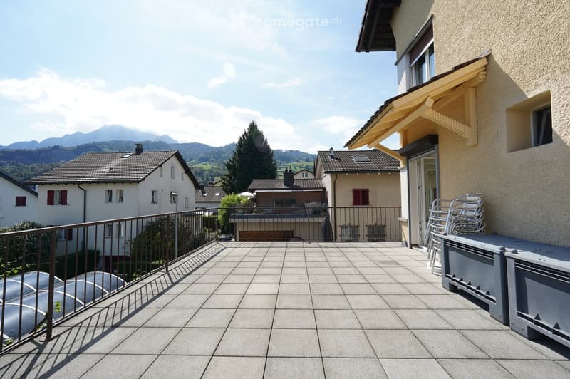 Balcony with tiled floor, metal railing, and outdoor furniture including stacked chairs and a small table.