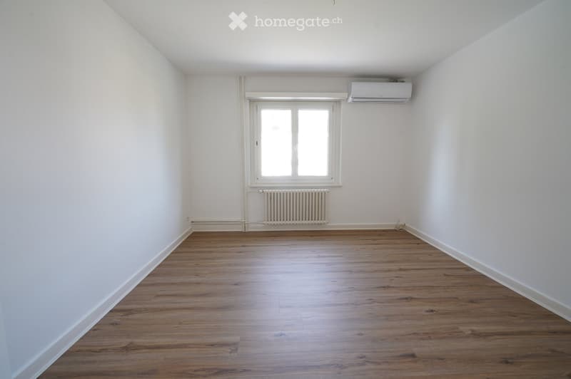 Empty room with wooden flooring, white walls, a window, a radiator, and an air conditioning unit on the wall.