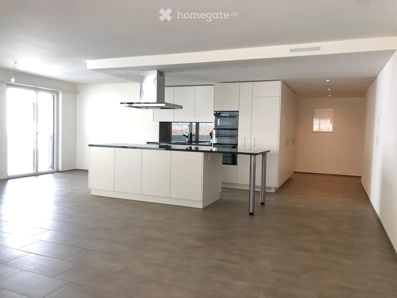Modern kitchen with white cabinets, a central island, built-in oven, and range hood. The space features tiled flooring and large windows allowing natural light.