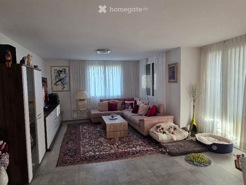Living room with a large sectional sofa, coffee table, side table with a lamp, picture frames on the wall, and decorative vases. There are also dog beds and toys visible.