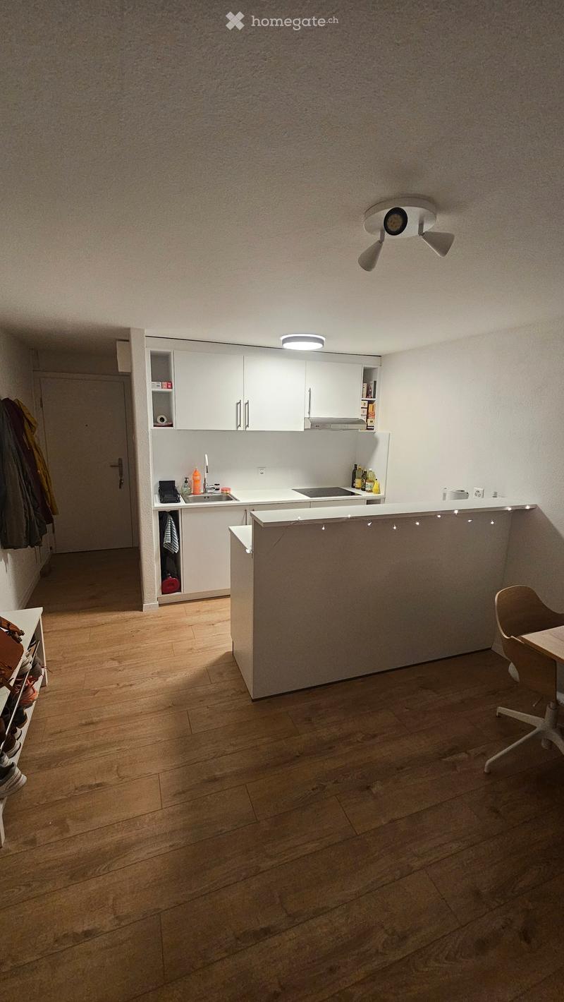 Modern kitchen with white cabinets, a central island, and wooden flooring. Includes a sink, faucet, and a small seating area with a chair and table.