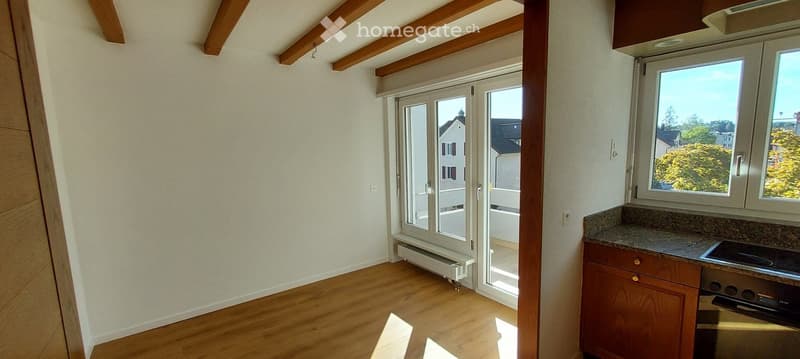 Empty room with wooden flooring, white walls, large windows, and a sliding glass door leading to a balcony.