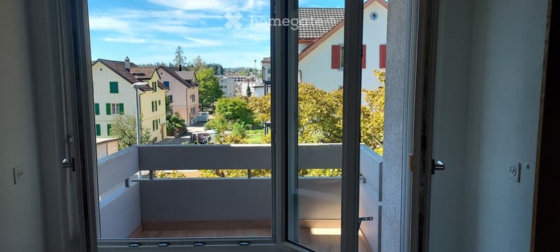 Open balcony with wooden flooring, white railings, and a scenic view of a residential neighborhood with houses, trees, and a clear blue sky.