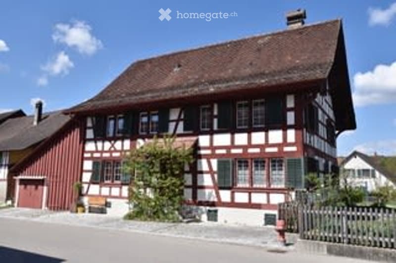 Traditional Swiss house with a red and white timber-framed facade, multiple windows, and a pitched roof.