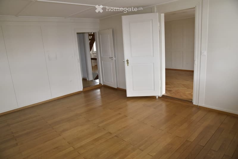 Empty room with wooden flooring and white walls, featuring several open doors leading to other rooms.