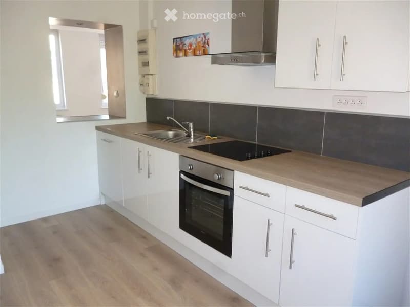 Modern kitchen with white cabinets, wooden countertop, stainless steel sink, faucet, and built-in oven. Features a sleek design with a dark backsplash and a range hood above the stove.