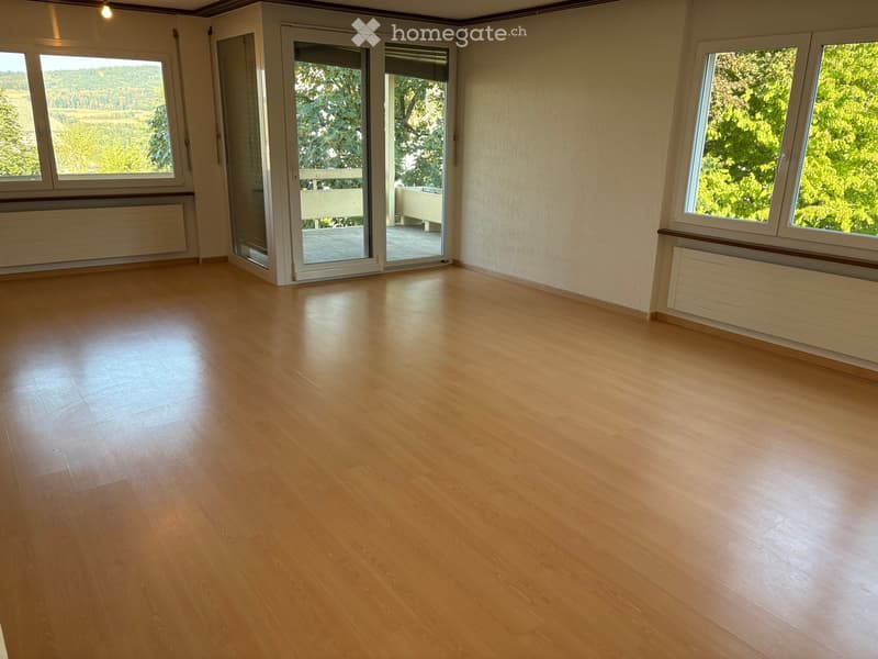 Empty room with wooden flooring, large windows, and a sliding glass door leading to a balcony.