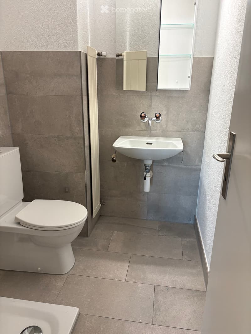 Modern bathroom with beige tiles, white toilet, sink, and mirror. Features a small window above the sink.