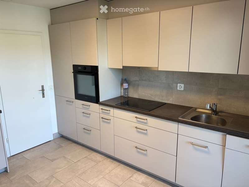 Modern kitchen with white cabinets, stainless steel sink, oven, and countertop.