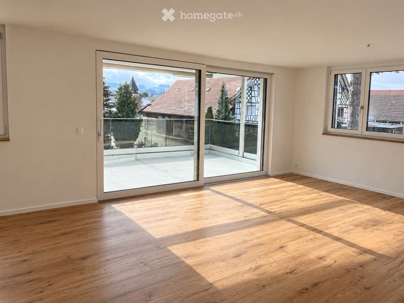 Empty room with wooden flooring, large sliding glass doors leading to a balcony, and a window on the right side.