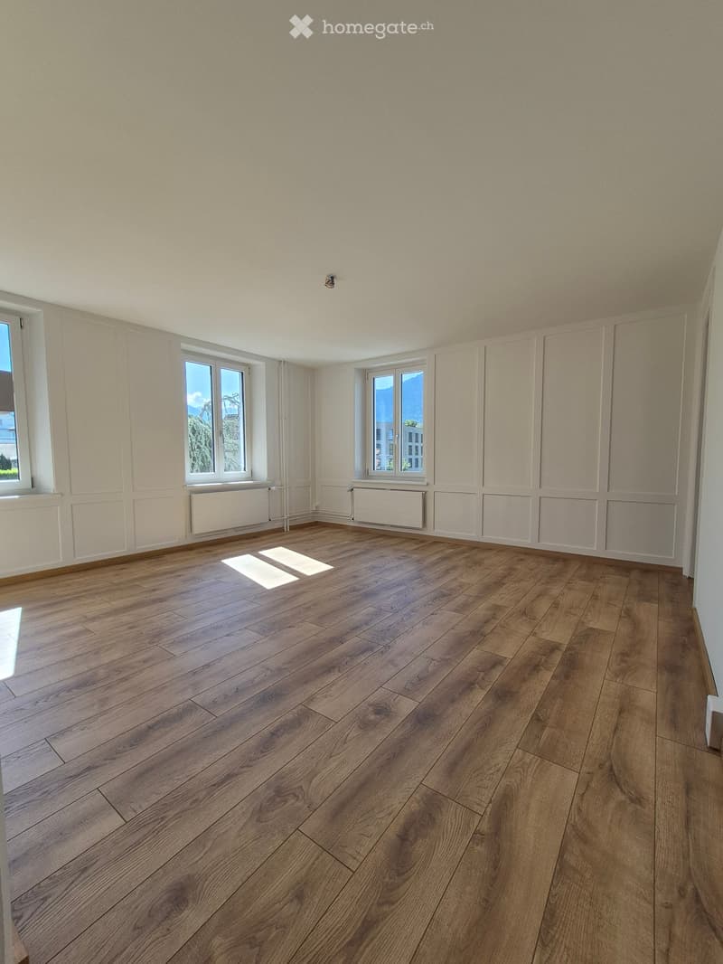 Empty room with wooden flooring, white walls, and large windows offering a view of the outdoors.