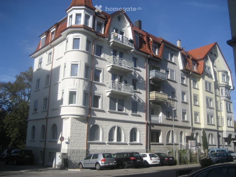 5 story white apartment building, red roof, arched windows, balconies, multiple cars parked in front