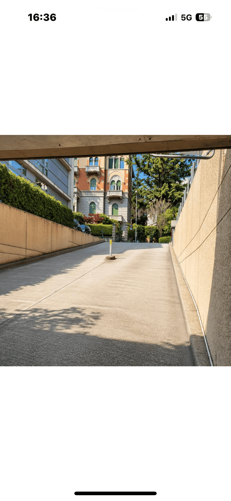 A narrow, paved pathway flanked by modern buildings and greenery, leading towards a historic building with ornate architecture.