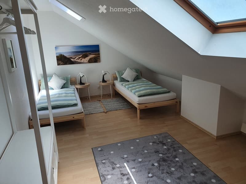 Cozy attic bedroom with wooden floors, two single beds, nightstands, lamps, and a large painting on the wall.