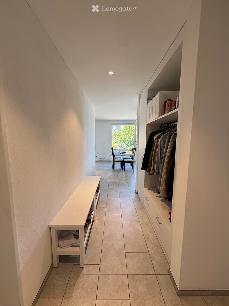 A modern hallway with built-in storage, a shoe rack, and a small dining area visible at the end.
