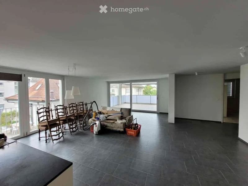 Bright, open living and dining area with large windows and a balcony. Includes a dining table with chairs, a sofa, and a lamp.