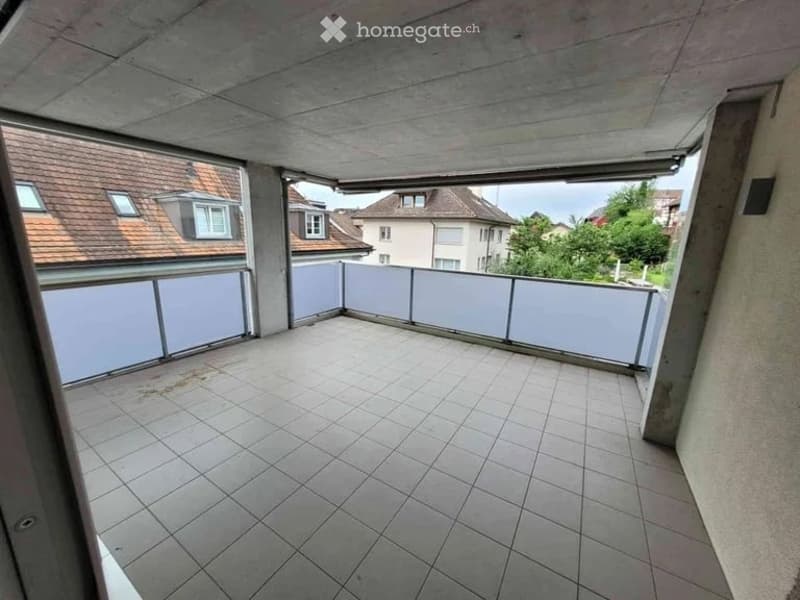 Empty balcony with tiled floor and white railing, overlooking neighboring houses and greenery.