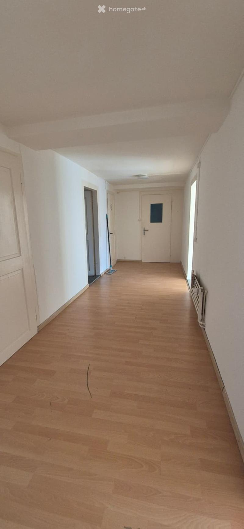 Empty hallway with wooden flooring, white walls, and several doors leading to rooms.