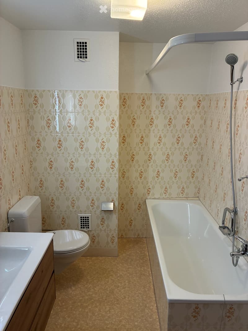 Bathroom with floral-patterned tiles, a bathtub, toilet, sink, and a showerhead on the wall.