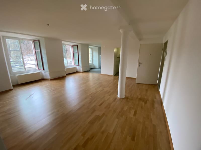 Empty room with wooden flooring, large windows, and a white column. No furniture or equipment present.
