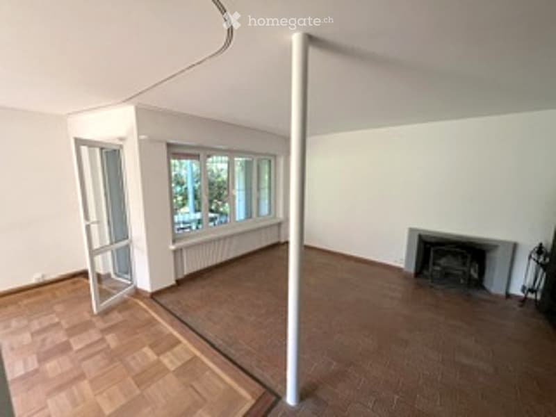 Empty room with wooden flooring, white walls, large windows, and a fireplace. No furniture or equipment present.