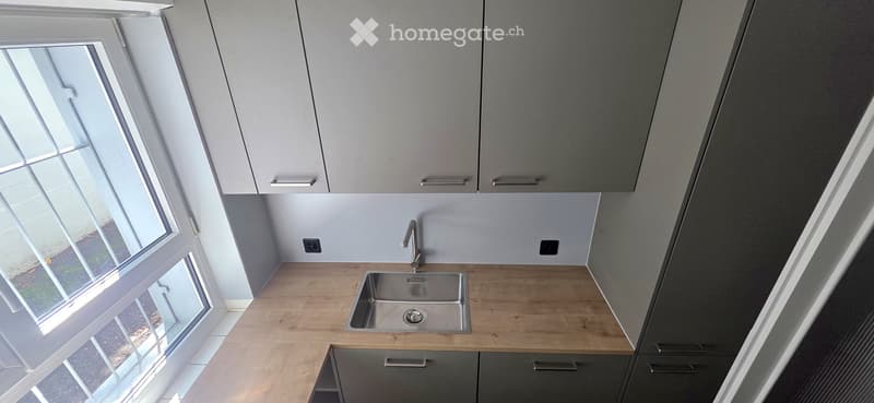 Modern kitchen with light wooden countertops, stainless steel sink, and grey cabinets.