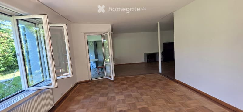Empty room with wooden flooring, large windows, and an open doorway leading to another room.