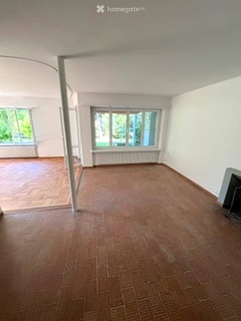 Empty room with wooden flooring, white walls, large windows, and a radiator. No furniture or equipment present.