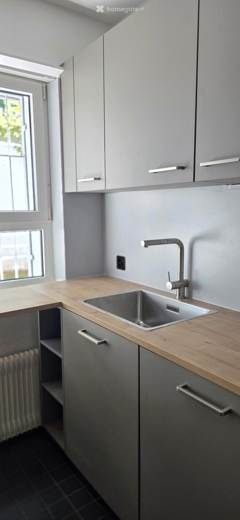 Modern kitchen with grey cabinets, wooden countertop, stainless steel sink, and faucet.
