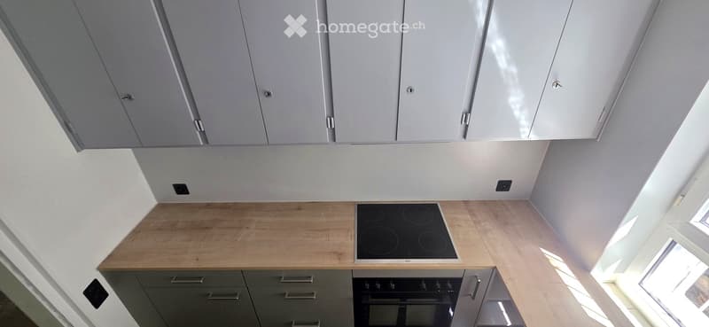 Modern kitchen with light grey cabinets, wooden countertops, and built-in appliances including an induction stove and oven.
