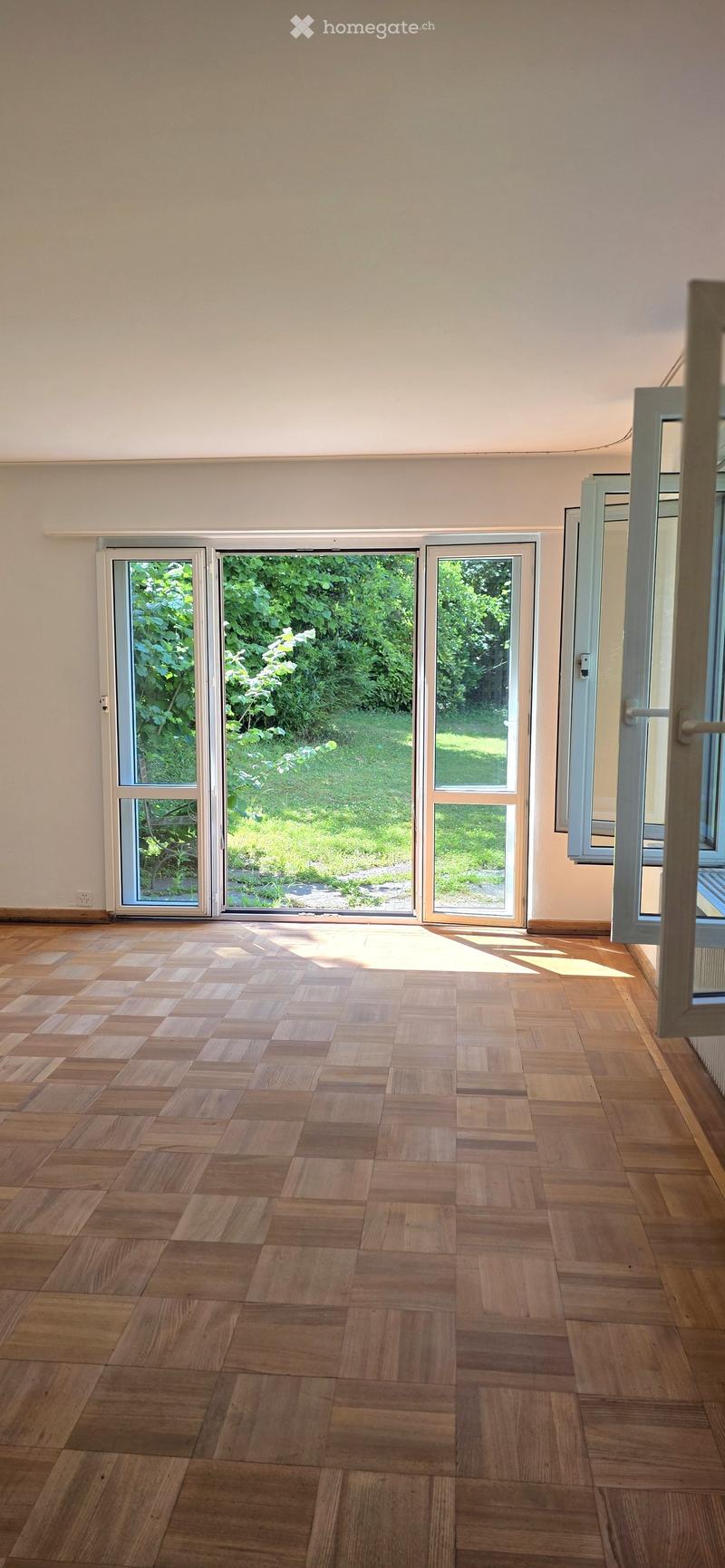Empty room with wooden flooring and large sliding glass doors leading to a green outdoor area.
