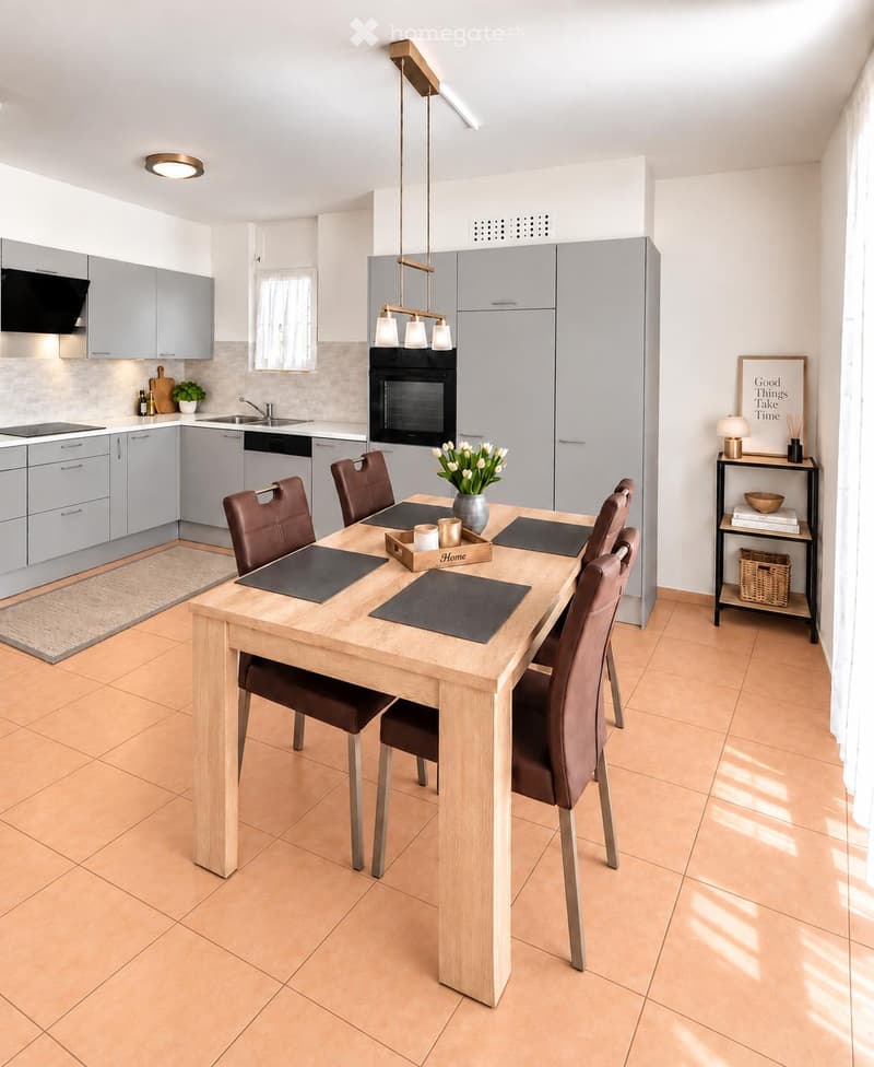 Modern kitchen with grey cabinets, a wooden dining table surrounded by brown chairs, a vase with white flowers, and a pendant light fixture.