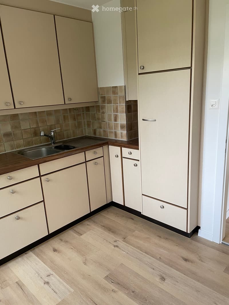 Modern kitchen with light wood cabinets, tiled backsplash, and wooden flooring.