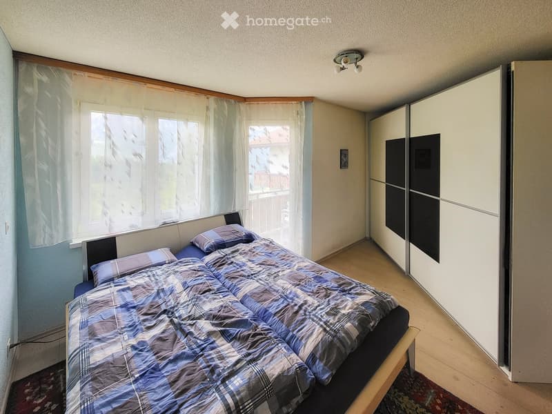Bedroom with a double bed, plaid duvet, pillows, a large wardrobe, and a window with sheer curtains.