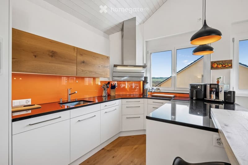 modern kitchen with white cabinets, orange glass backsplash, black countertops, wooden floor, large windows, kitchen appliances