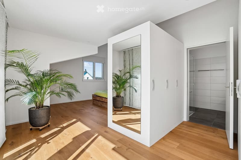 modern room with wooden floor, white walls, large mirror, potted plants, open door, small window, and a small bed